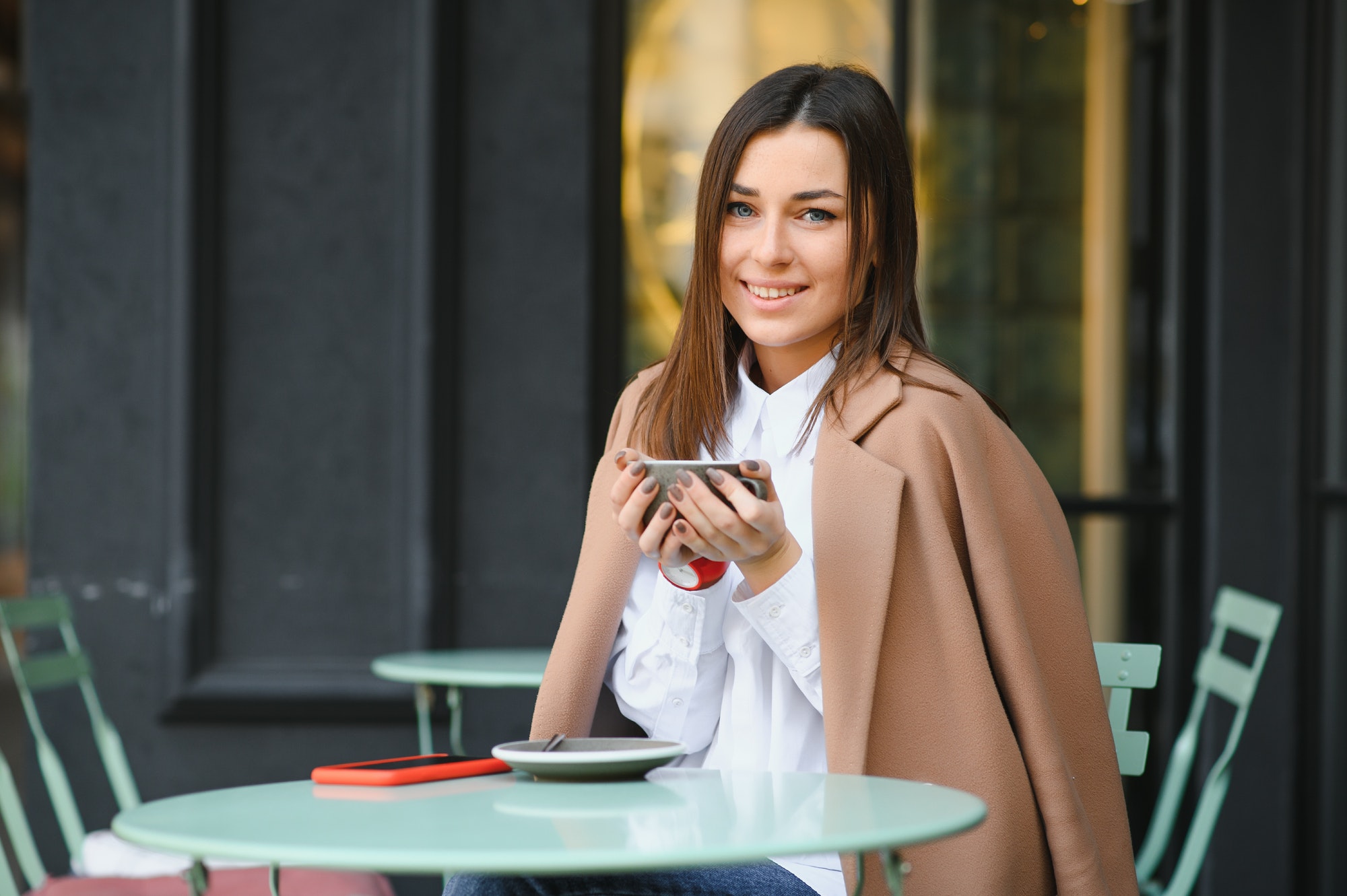 Young woman sitting outside the cafe with hot beverage